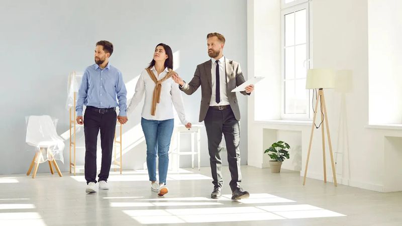 تصویر یک مشاور املاک که خانه ای را به خریداران نشان می‌دهد.